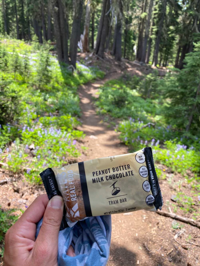 Holding A Kate's Chocolate Peanut Butter Energy Bar Outdoors On The Trail