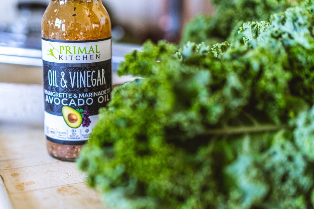 Bottle Of Primal Kitchen Oil & Vinegar Vinaigrette & Marinade Made With Avocado Oil Next To Leafy Kale For Keto Kale Salad With Avocado Oil And Vinegar Dressing Primal Kitchen Recipe