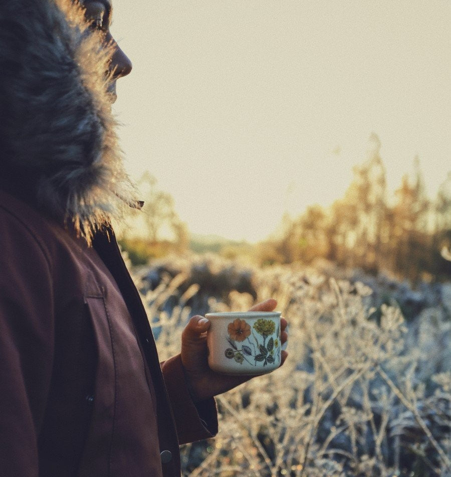 Woman Outdoors In Coat Holding Metal Floral Camp Mug Of Organic Coffee